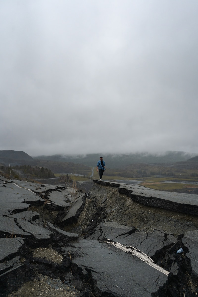 man in blue jacket standing on rock formation during daytime pondering if he should get earthquake insurance